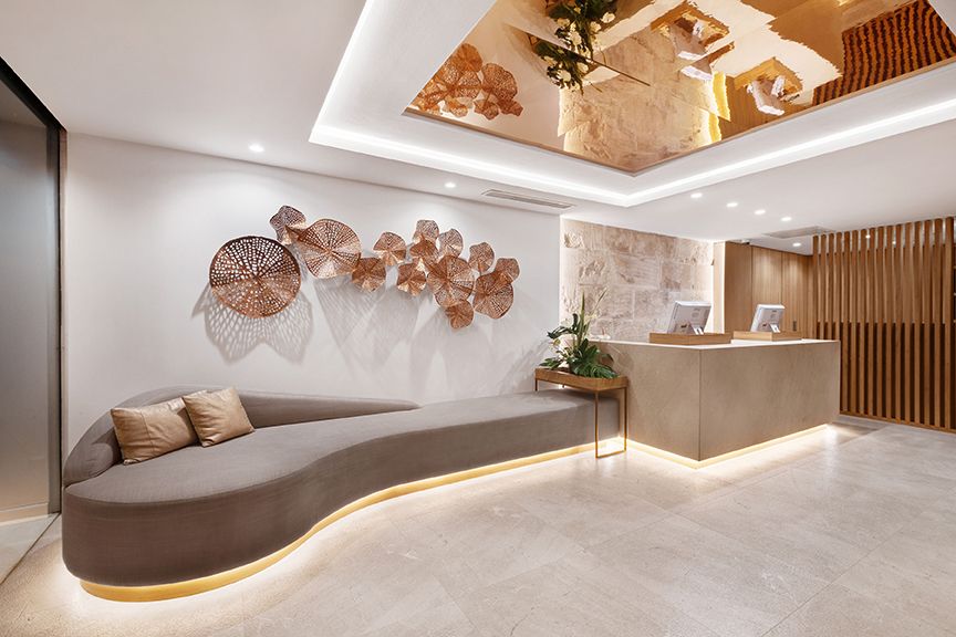 Reception lobby with a curved lounge sofa, copper wall art and a wood-slat front desk