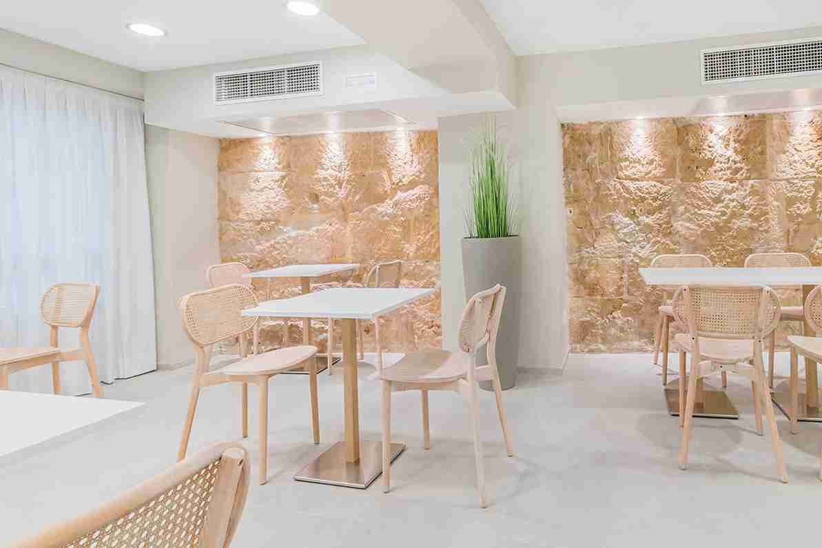 Breakfast room with rattan chairs, white tables and a backlit stone accent wall
