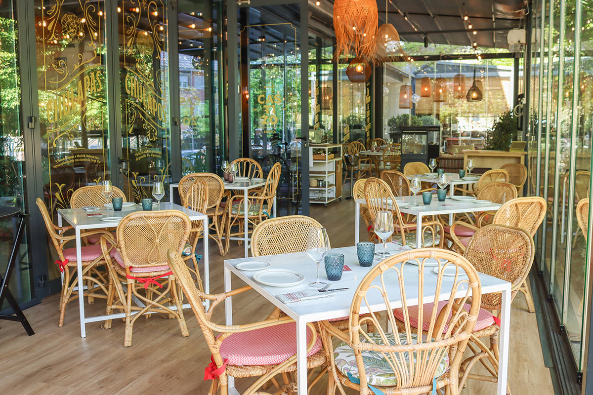 The glass-enclosed Castizo terrace with rattan chairs and set tables, 'Castizo' and 'Chulapas Chulapos' lettering etched on the glass partitions.