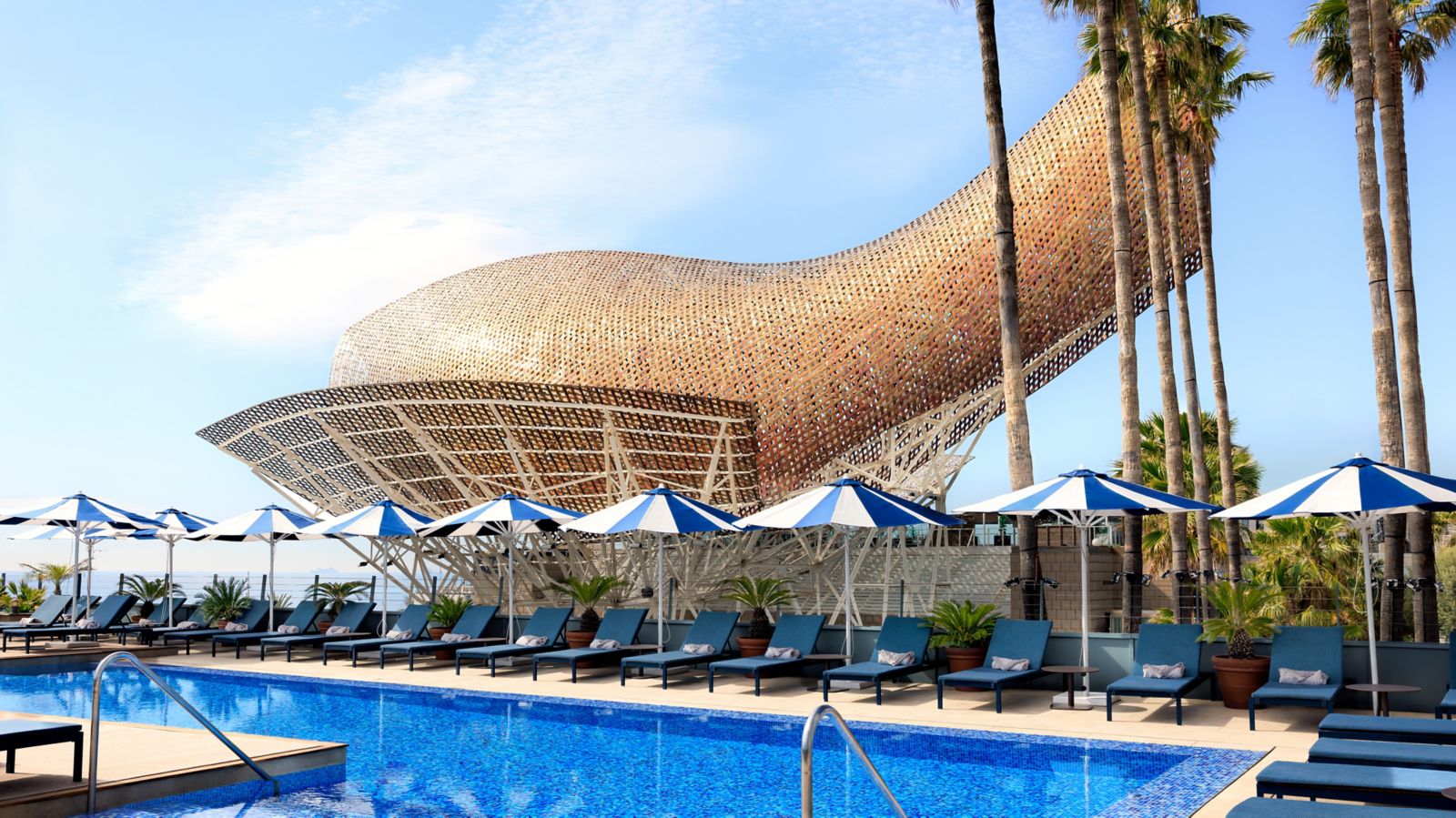 Rooftop pool deck with striped umbrellas beside the Frank Gehry fish sculpture