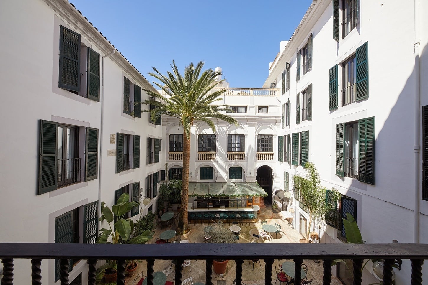 View from a balcony over the hotel's interior courtyard with a tall palm, outdoor tables and a bar