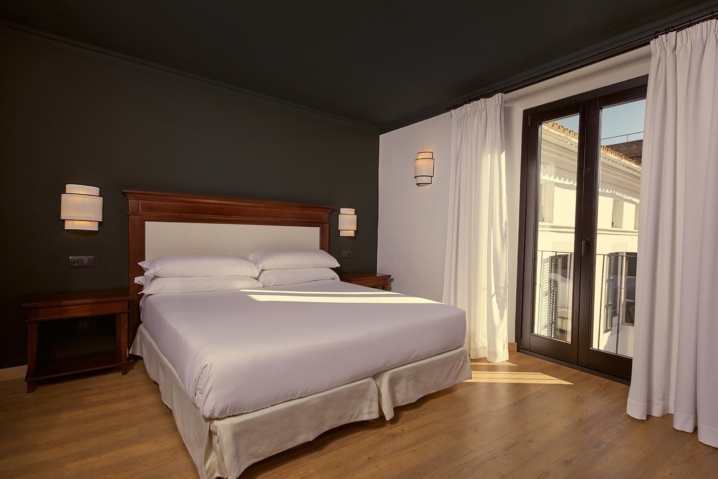 Guest room with dark walls, a wood-framed bed and a Juliet balcony over the street