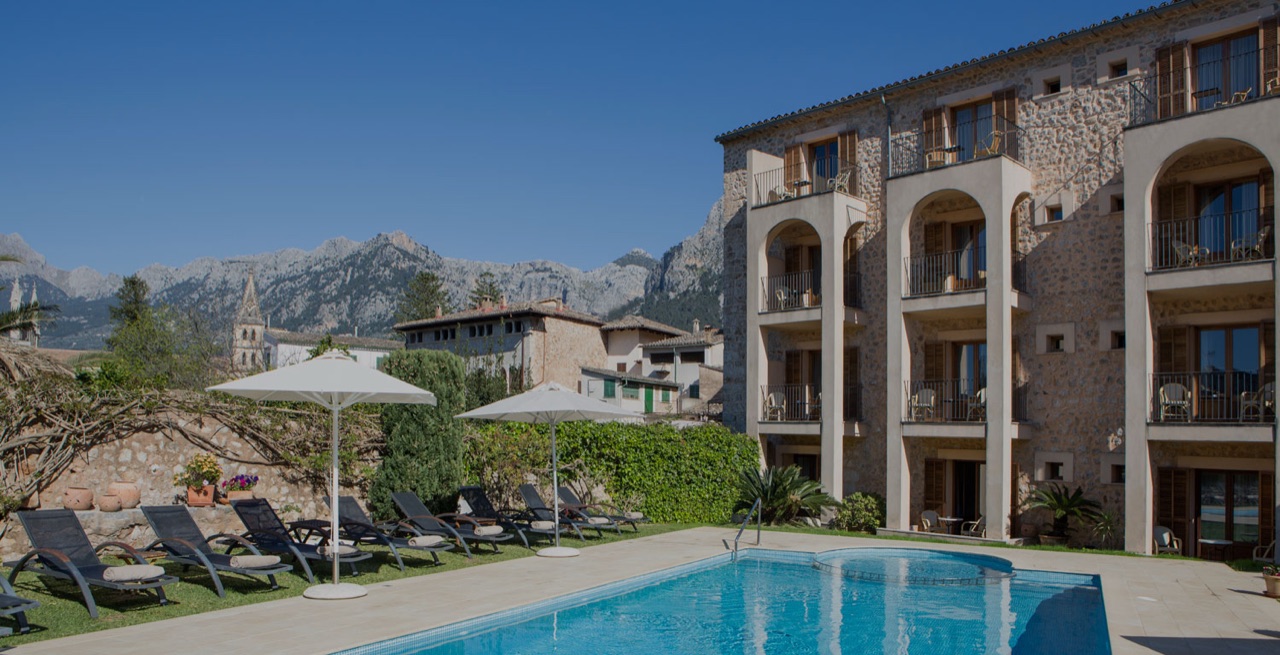 Stone facade of Hotel Ca'l Bisbe with balconies overlooking the outdoor pool and Sóller's rooftops.