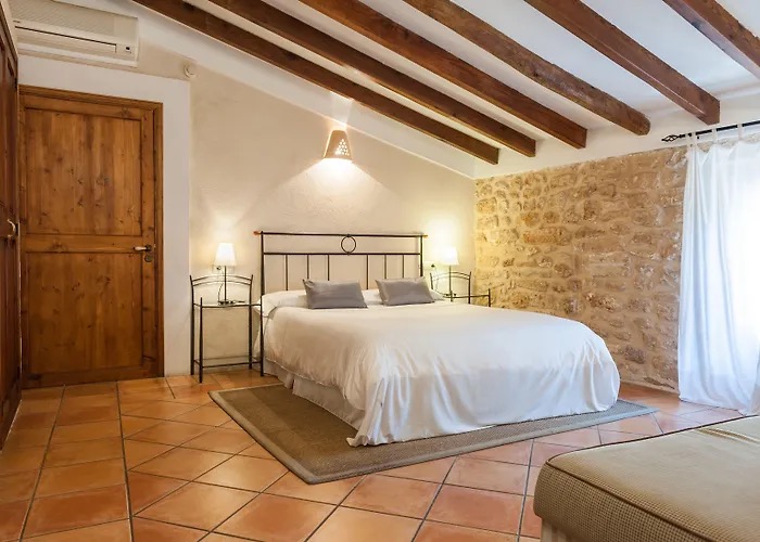 Beamed-ceiling bedroom with an exposed stone accent wall and a white made-up bed
