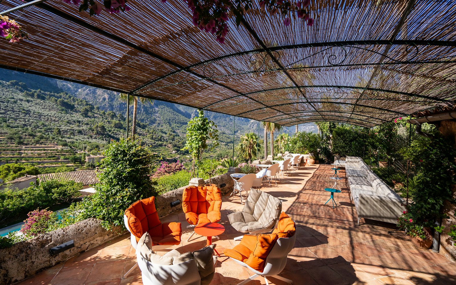 Cane-roofed terrace lounge with orange and cream armchairs overlooking the Sóller valley