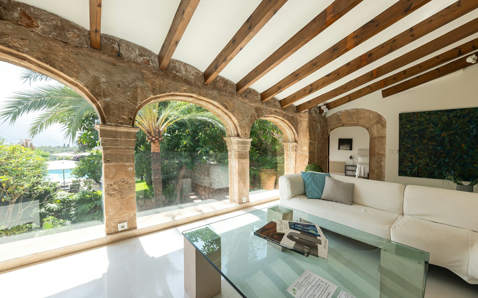 Stone-arched living room with a white sofa and glass coffee table, opening onto palm trees and the pool