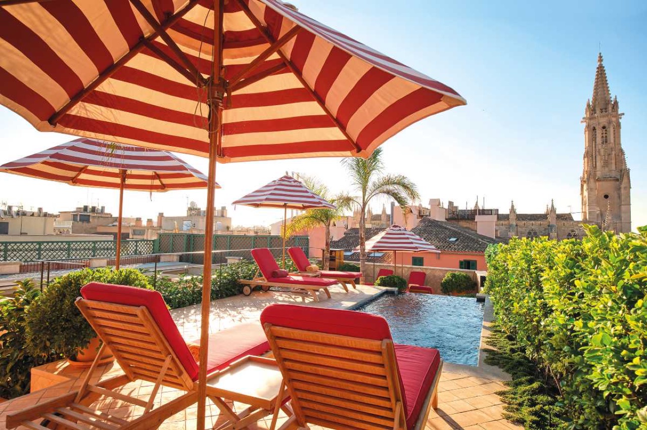 Rooftop pool with striped loungers and a view of Palma cathedral tower