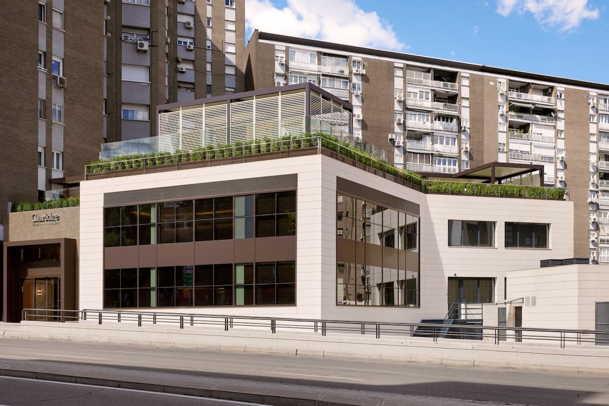 The white, modern facade of Hotel Claridge with its rooftop terrace planting, set against taller apartment blocks behind it.
