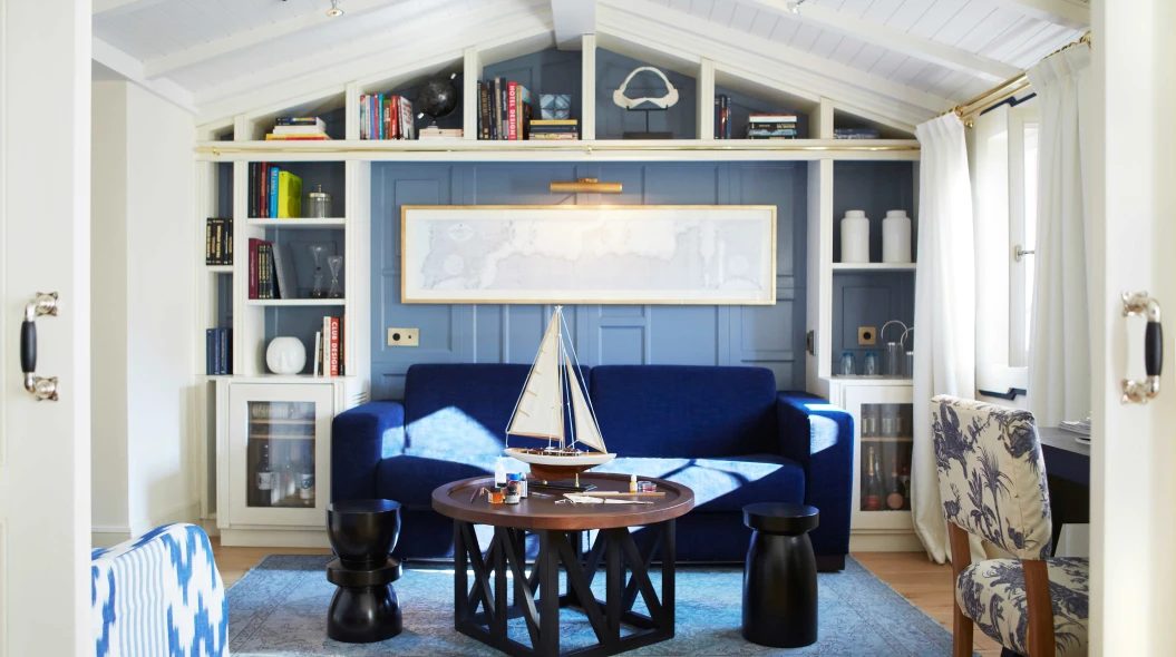 Suite Placa sitting room at Hotel Cort with a navy sofa, a model sailboat on the coffee table, and built-in bookshelves under a vaulted wood-beam ceiling