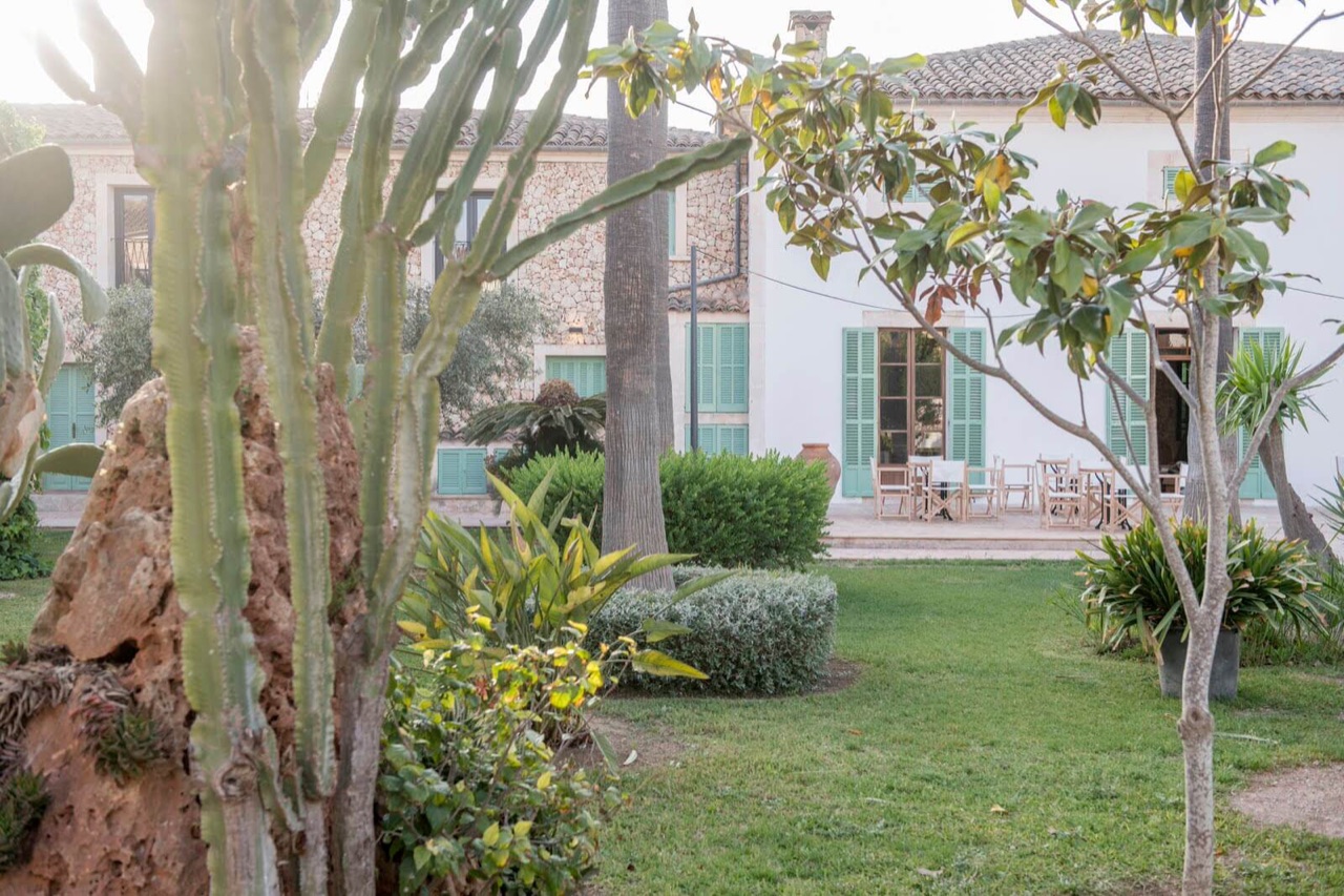 The hotel's white stone building seen across the garden lawn, with an outdoor dining terrace set with tables and chairs.