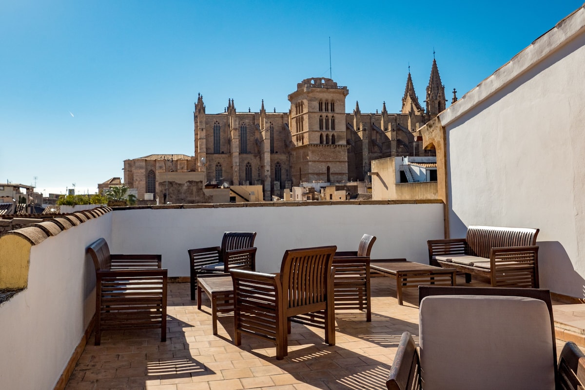 Rooftop terrace at Hotel Dalt Murada with wooden loungers and a view over the old town rooftops to Palma Cathedral