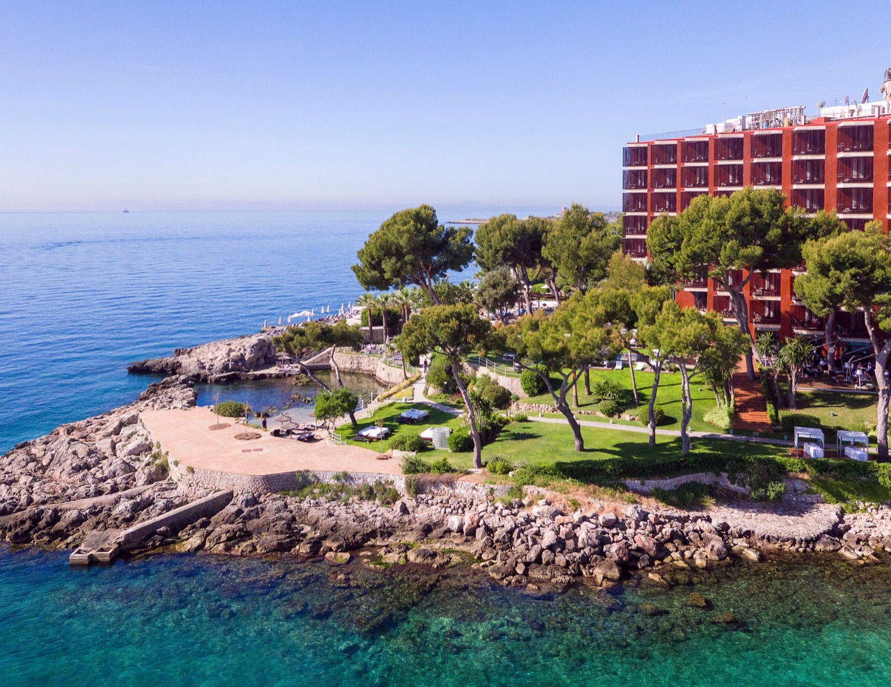 Aerial view of the hotel building on a rocky cove with pine gardens