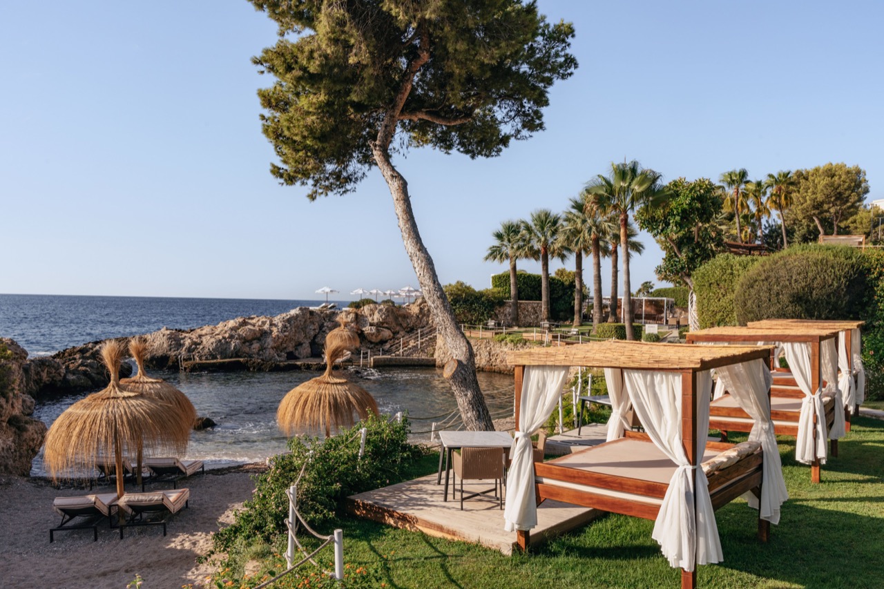 Canopied daybeds and straw parasols on the waterfront lawn