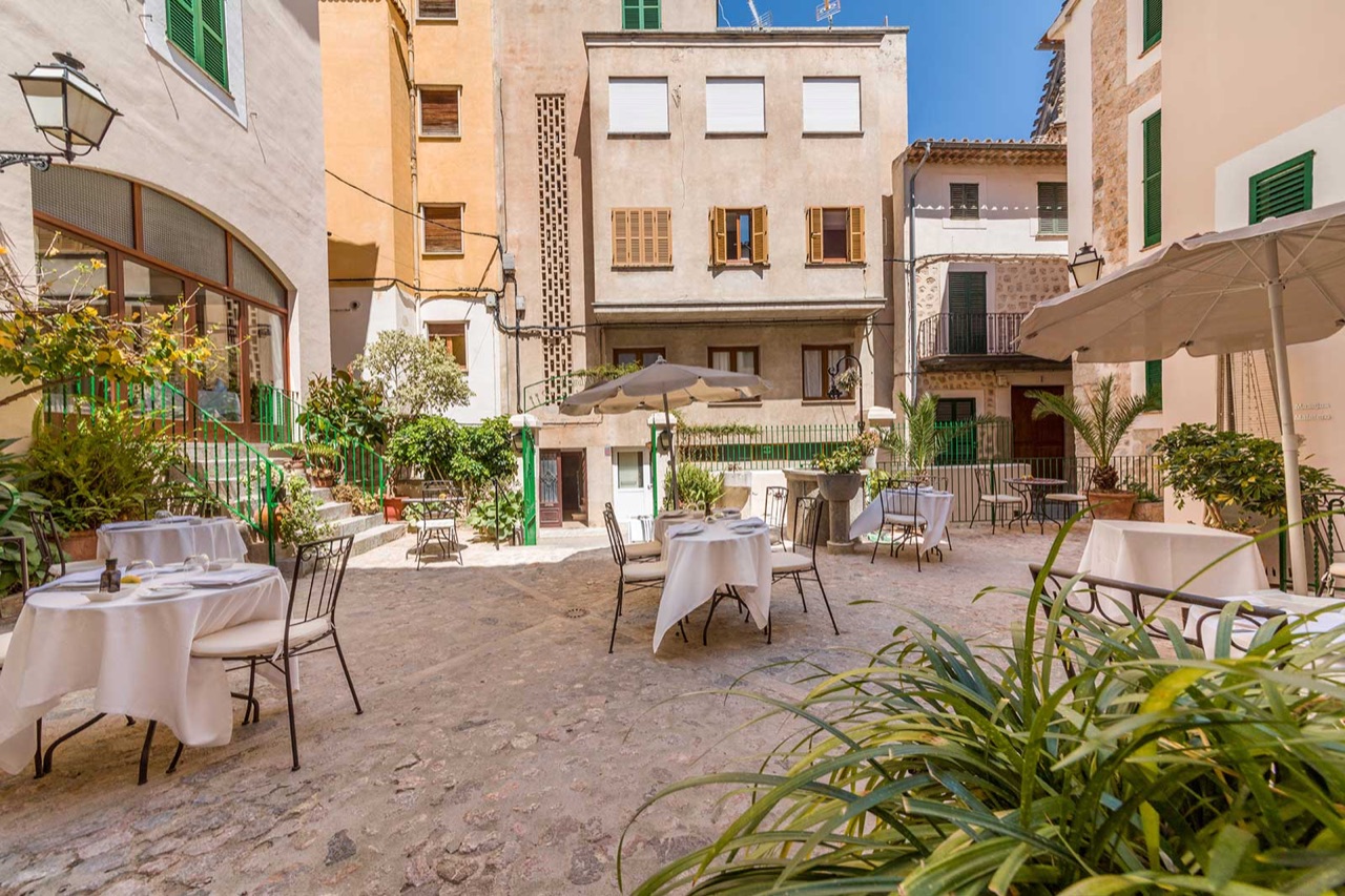 The cobbled courtyard terrace of Restaurant Ca's Pentinadó, with white-clothed tables, umbrellas and Sóller's old-town buildings behind.