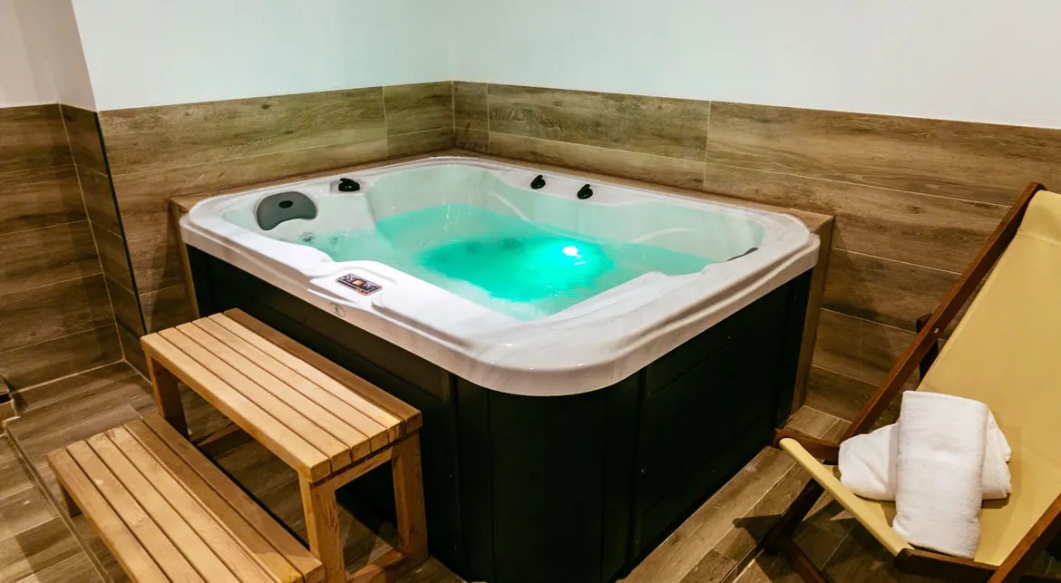 The hotel's small jacuzzi lit turquoise, with a wooden step bench and a deck chair beside it.