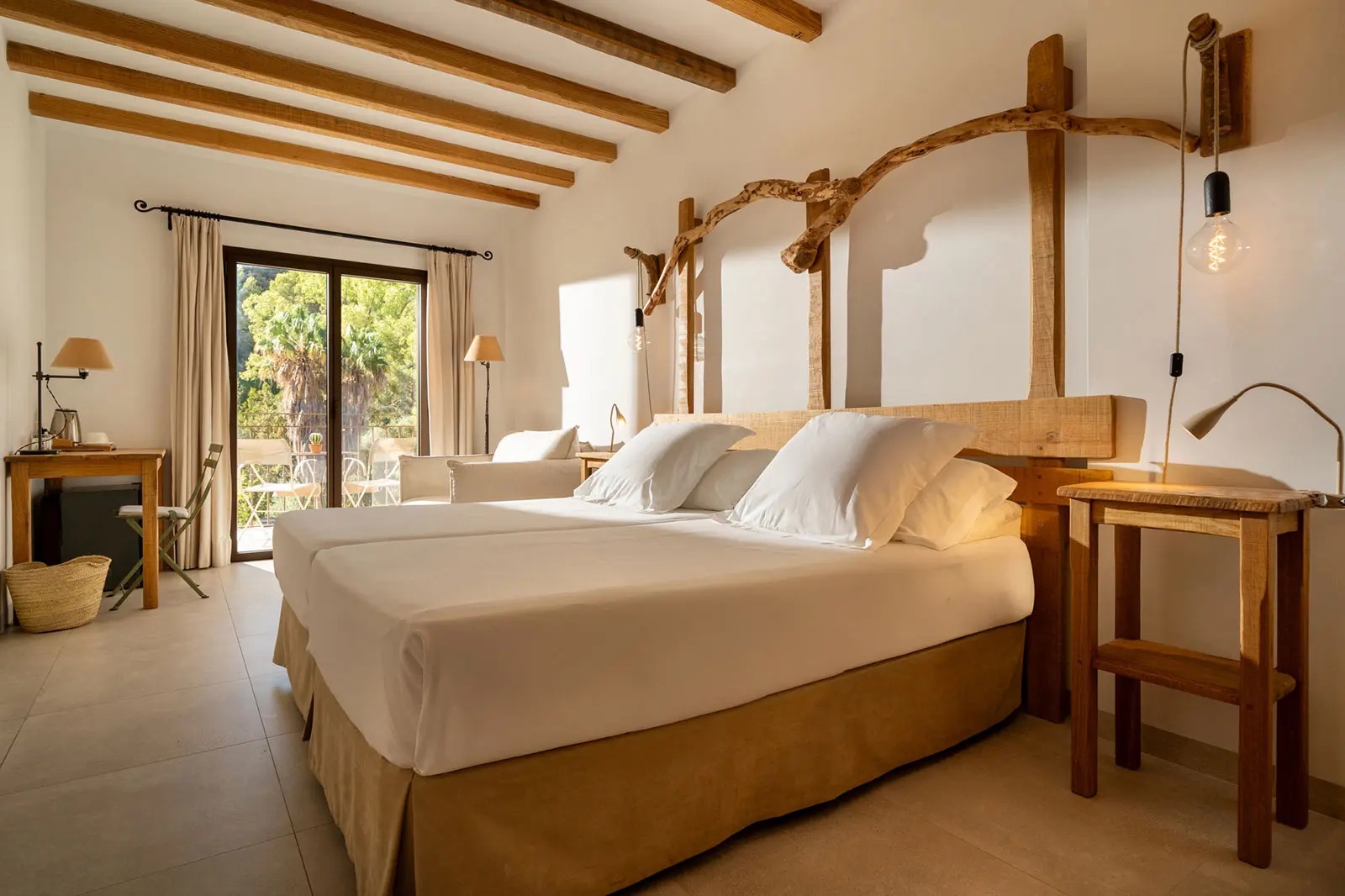 Guest room with a wood-beamed ceiling, a driftwood headboard and glass doors opening onto a private terrace