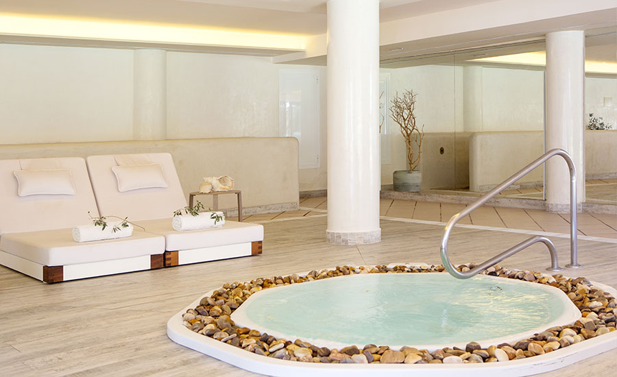 Spa whirlpool tub ringed with river stones next to loungers in the indoor relaxation area