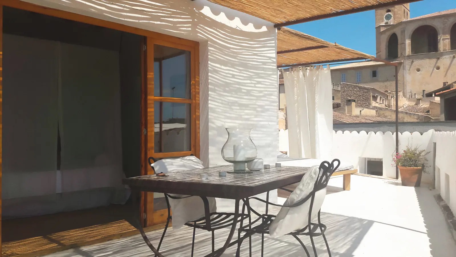 Rooftop terrace dining table shaded by a reed canopy, with views over Arta's rooftops to the parish church