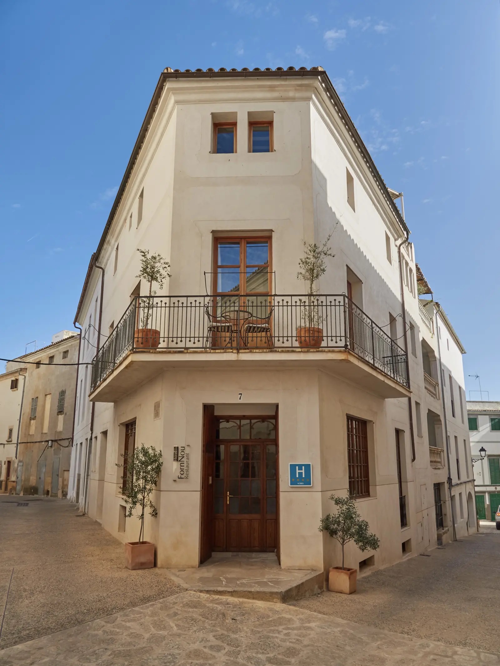 Corner facade of the hotel's historic building in Arta's old town, with wrought-iron balconies and the H hotel plaque by the entrance