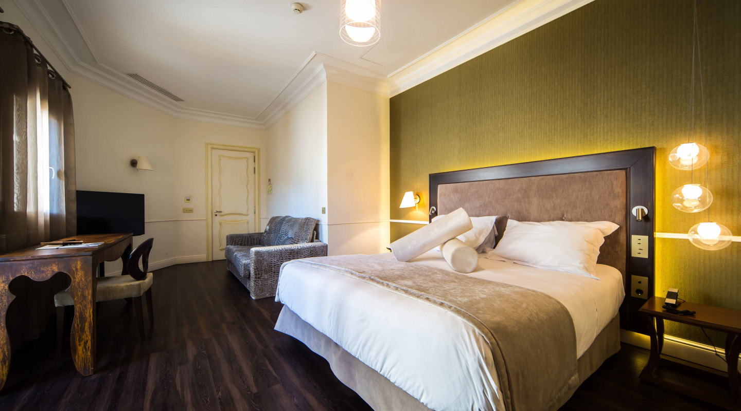 Junior Suite bedroom with an olive-green upholstered headboard, a leather armchair and dark wood flooring