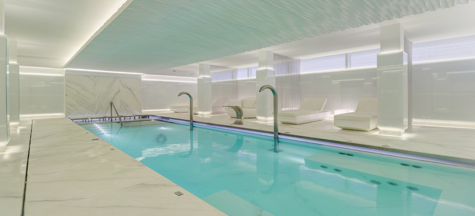 Indoor hydrothermal spa pool with marble surrounds and white loungers