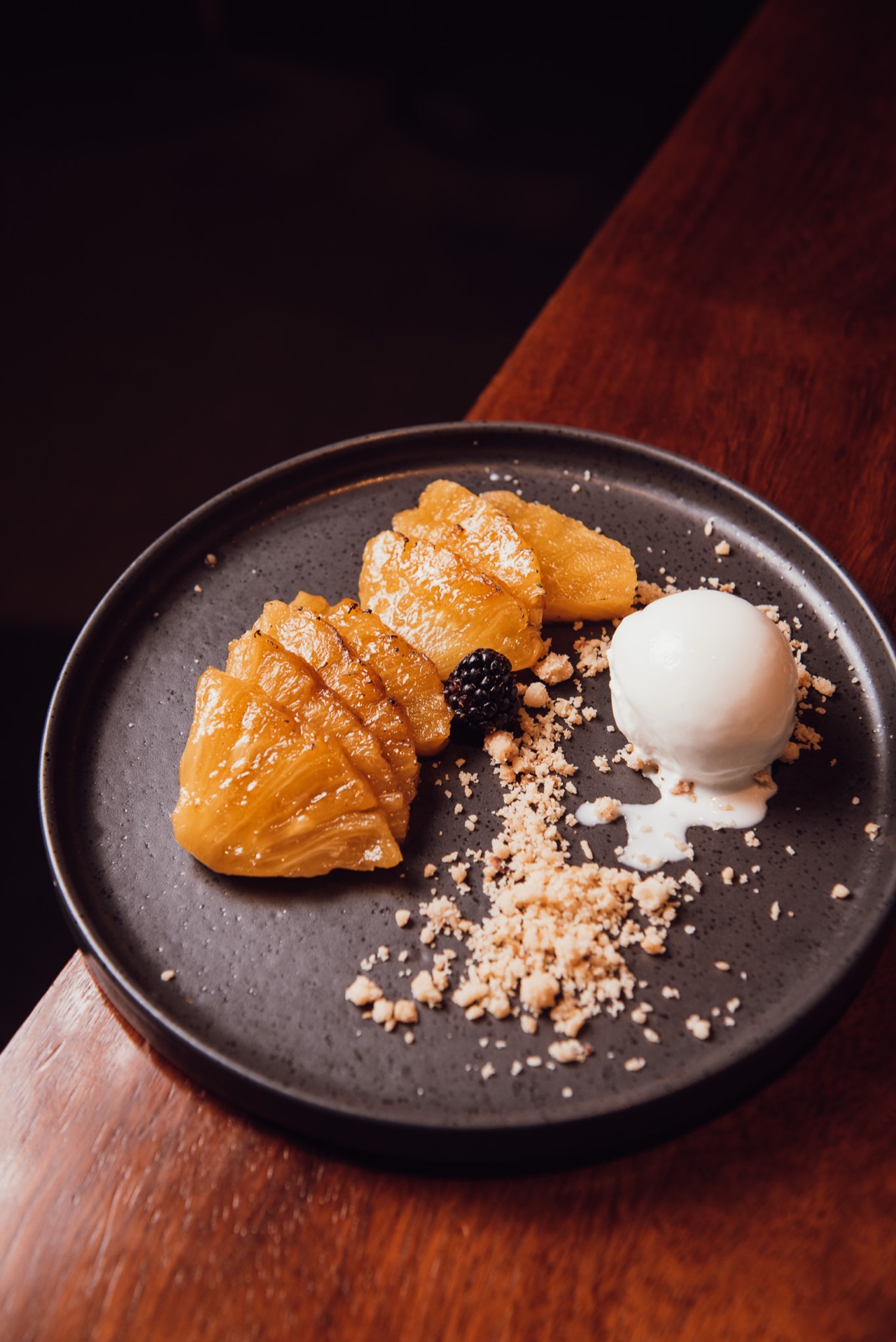 Dessert plate from El Telón with sliced caramelized pineapple, a blackberry, crumble and a scoop of white sorbet or ice cream.