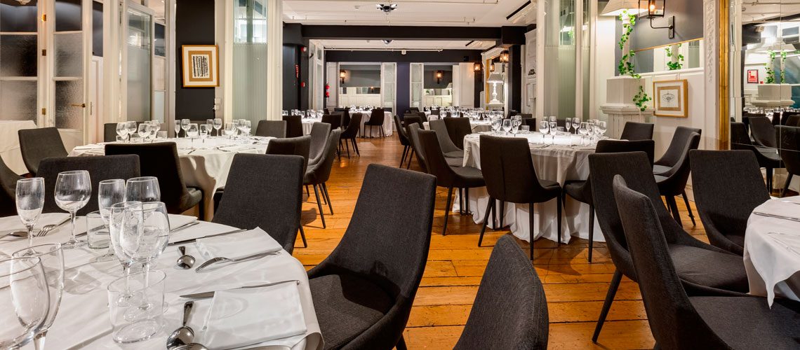 Private event dining room at Hotel Market set with round tables, white linens and dark upholstered chairs on a wood plank floor