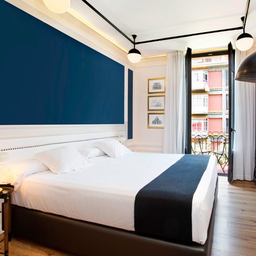 Double room at Hotel Market with a navy upholstered headboard wall, white bedding with a navy foot runner and French doors onto a balcony
