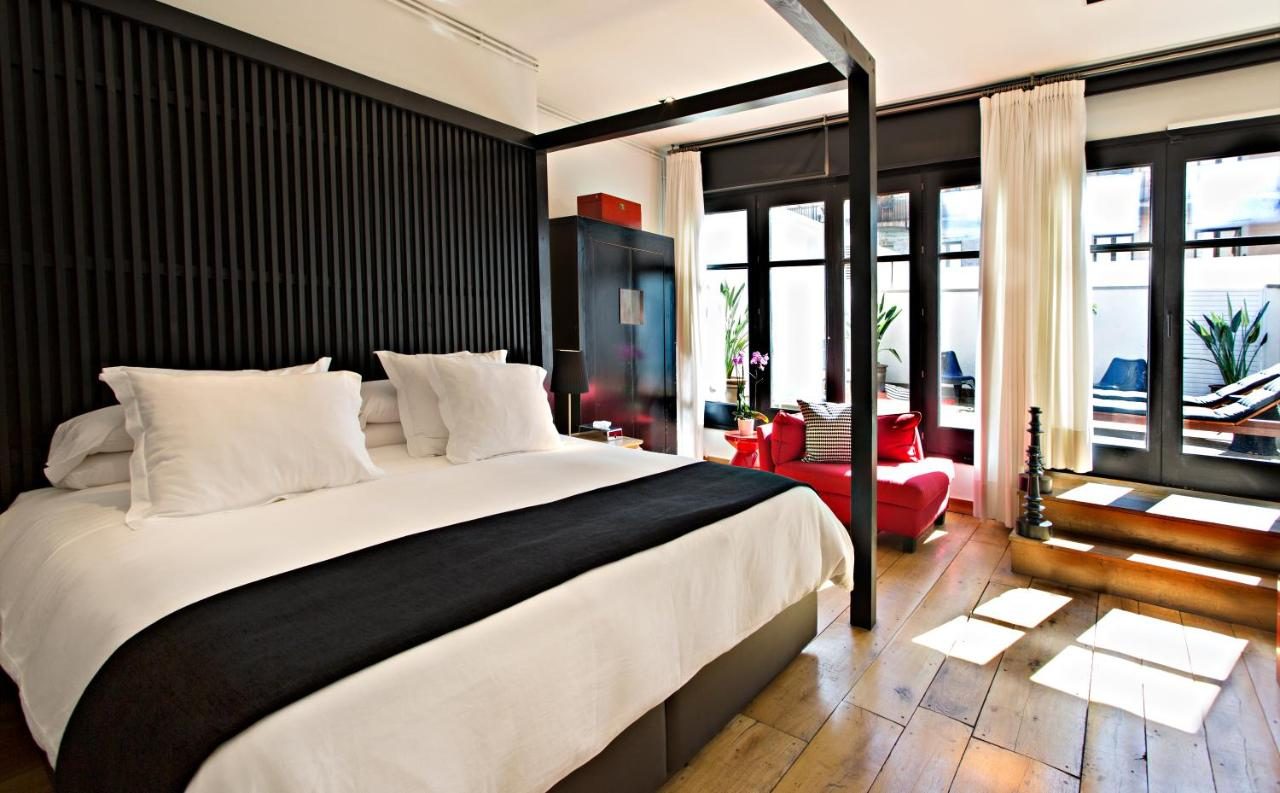 Junior Suite at Hotel Market with a dark wood slat headboard wall, a black four-poster bed frame, a red armchair and a private terrace with lounge chairs