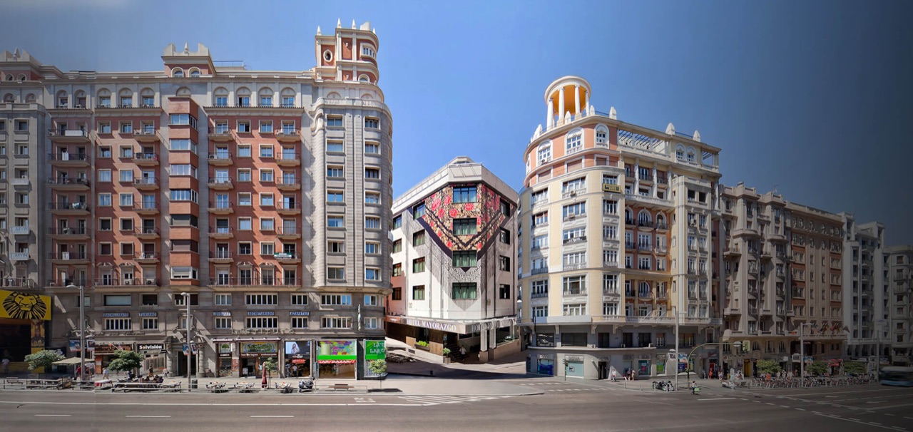 Narrow corner building on a Madrid street with a large manila-shawl style floral mural covering its upper facade and a HOTEL MAYORAZGO sign over the entrance, flanked by taller neighbouring buildings.