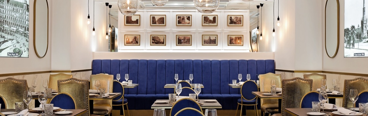 GastroVía 61 dining room with a long royal-blue banquette, gold-trimmed chairs, hanging glass pendant lights and rows of framed historic photos of Madrid plazas on the wall.