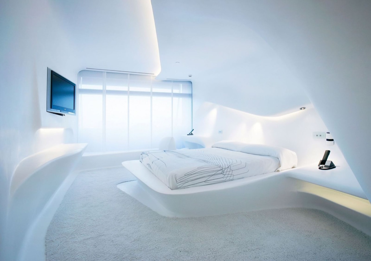 An all-white curved guest room with a sculptural floating bed and a wall of windows, designed by Zaha Hadid's Space Club concept.