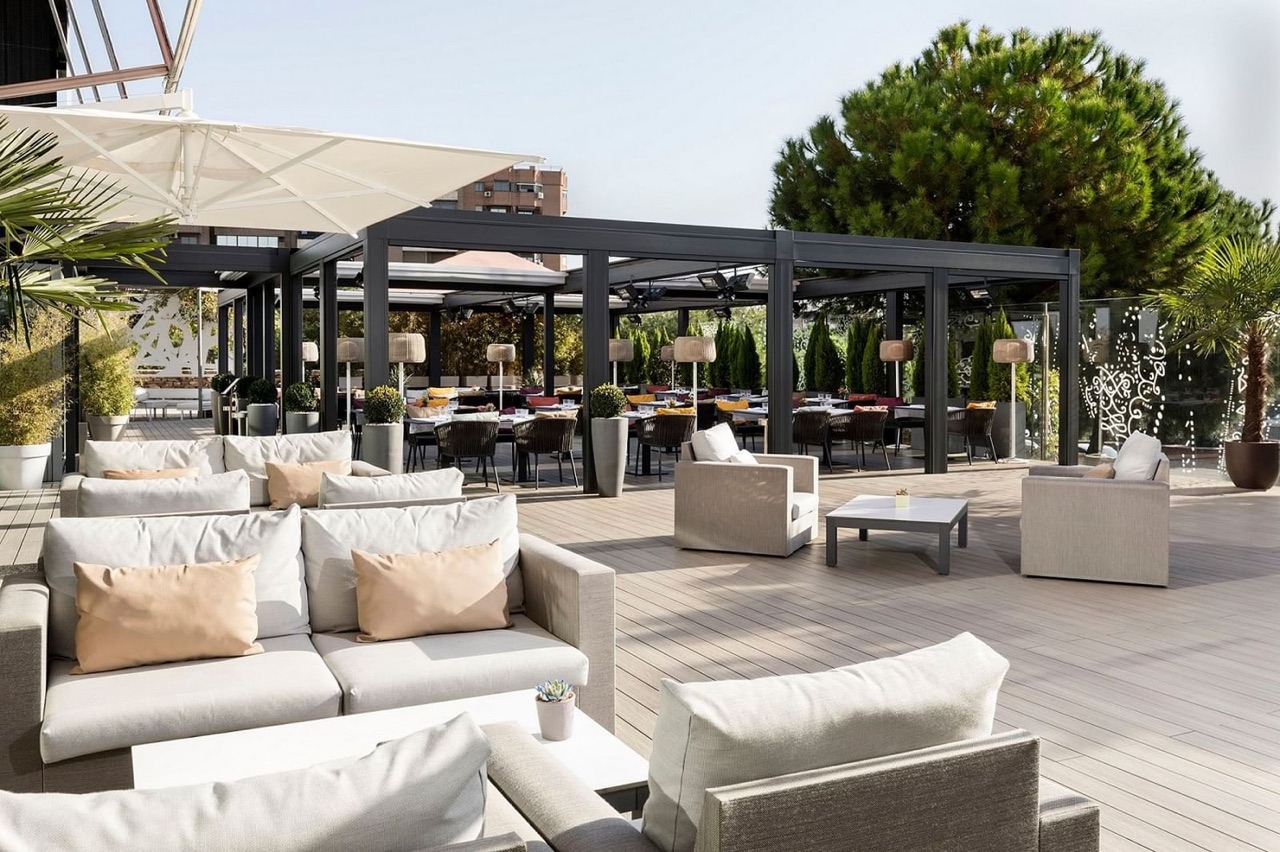Karrara Terrasse's outdoor lounge and dining area with white sofas, umbrellas and pine trees under a pergola.