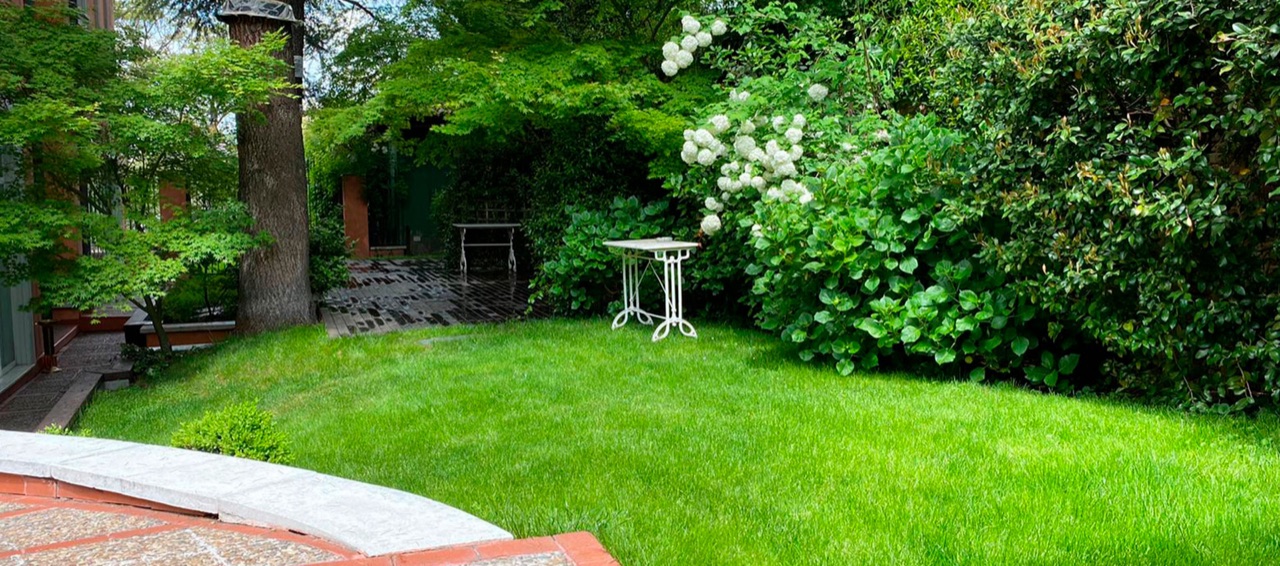 Manicured lawn and hedges in the hotel garden, with a small white side table and a stone-paved path in the foreground.