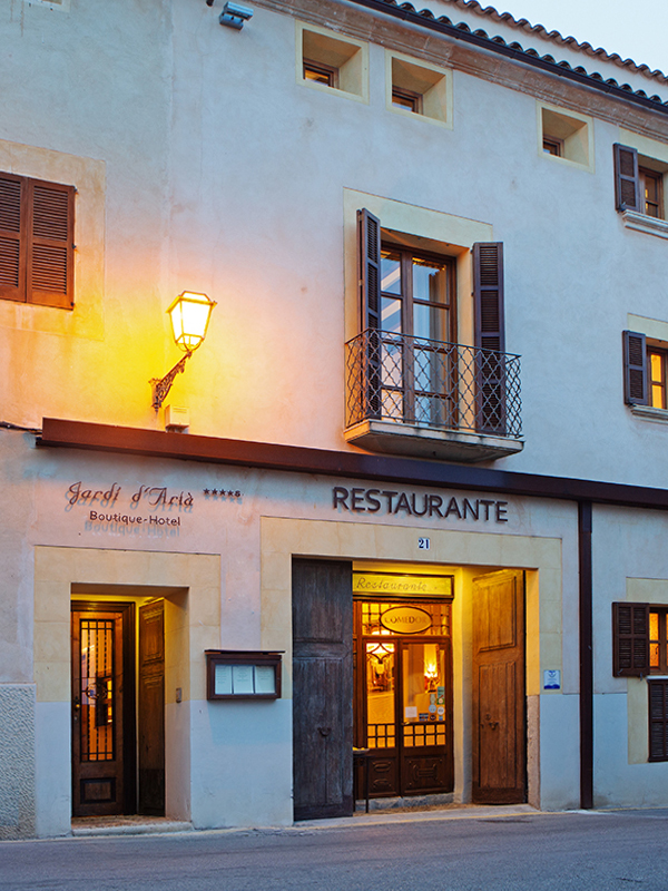 Twilight view of the hotel and restaurant facade in Artà's old town, with a lit balcony and lantern over the entrance