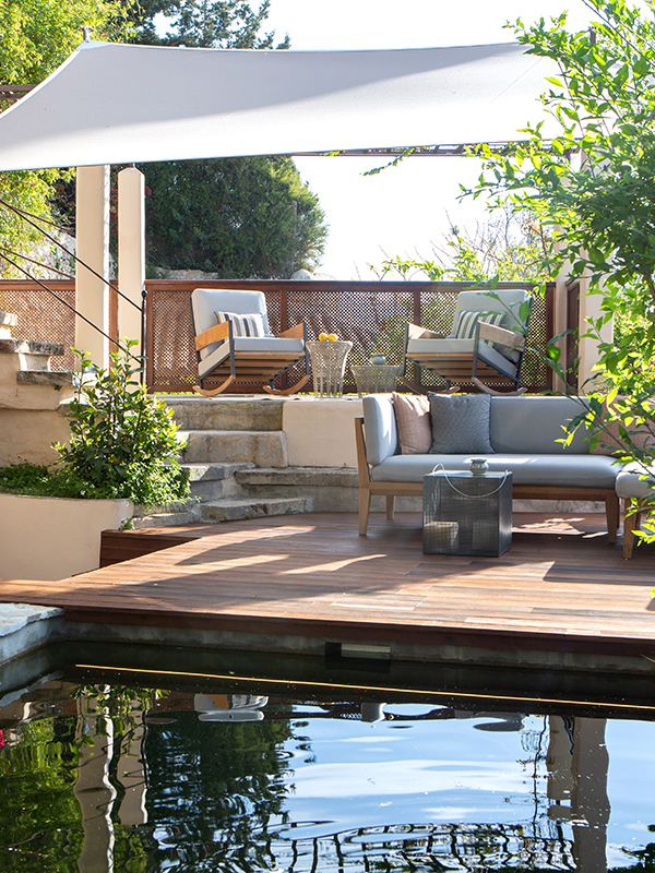 Wooden sun deck with lounge seating and a shade sail beside the pool