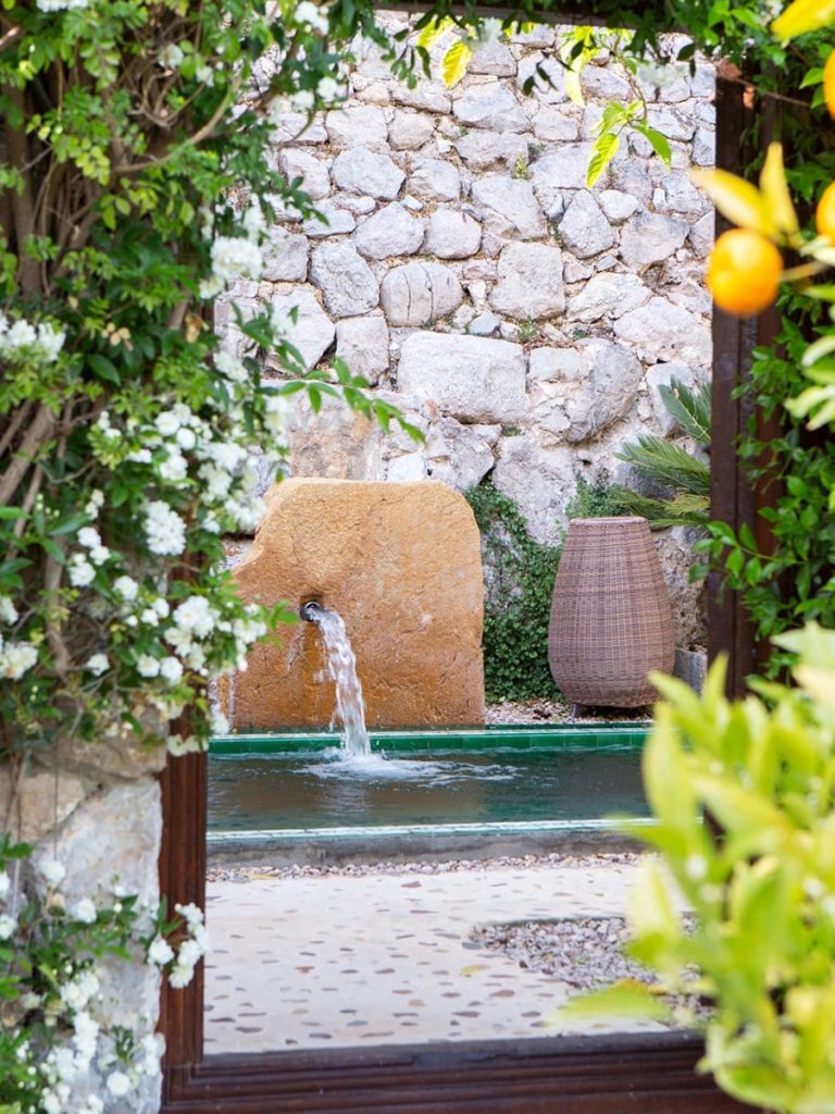 Garden pool with a stone fountain, framed by flowering vines and an orange tree