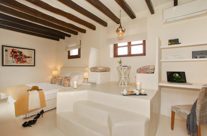 Guest room with exposed wood-beam ceiling, a raised platform bed and a small desk area