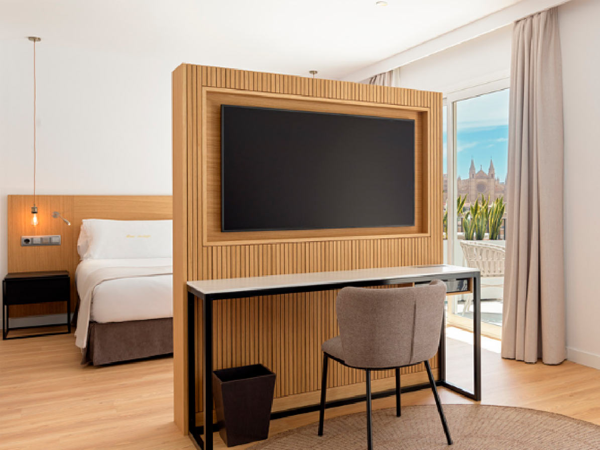 Hotel room with a wood-panelled TV wall, a bed and a desk, with Palma Cathedral visible through the balcony door.