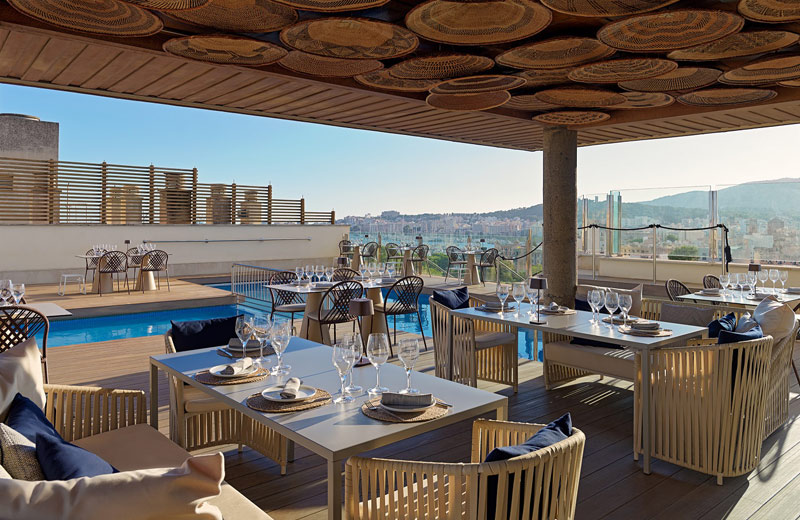 Rooftop terrace with dining tables set beside the pool, overlooking the city and hills.