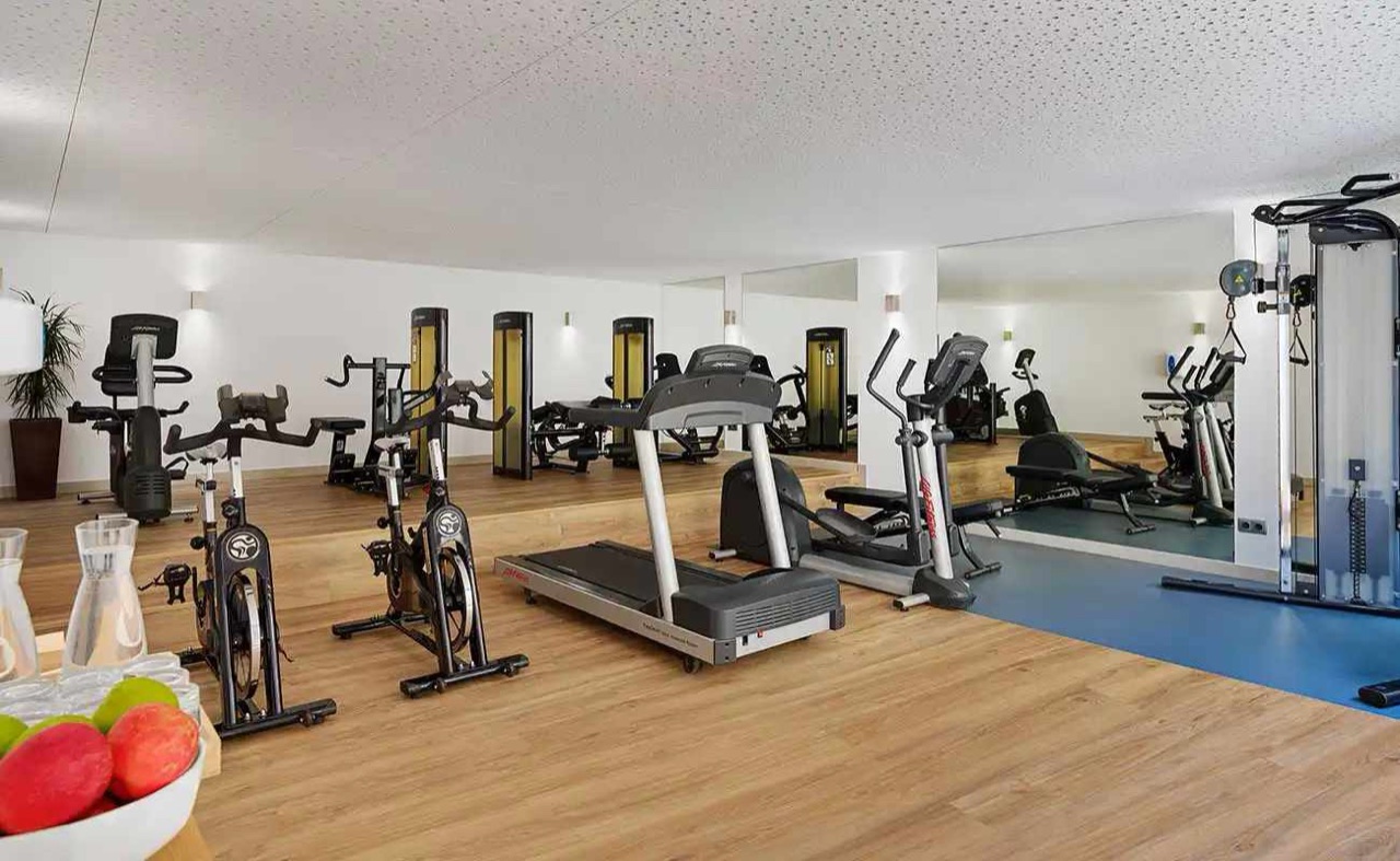 Hotel gym with treadmills, exercise bikes and strength machines on a wood floor.