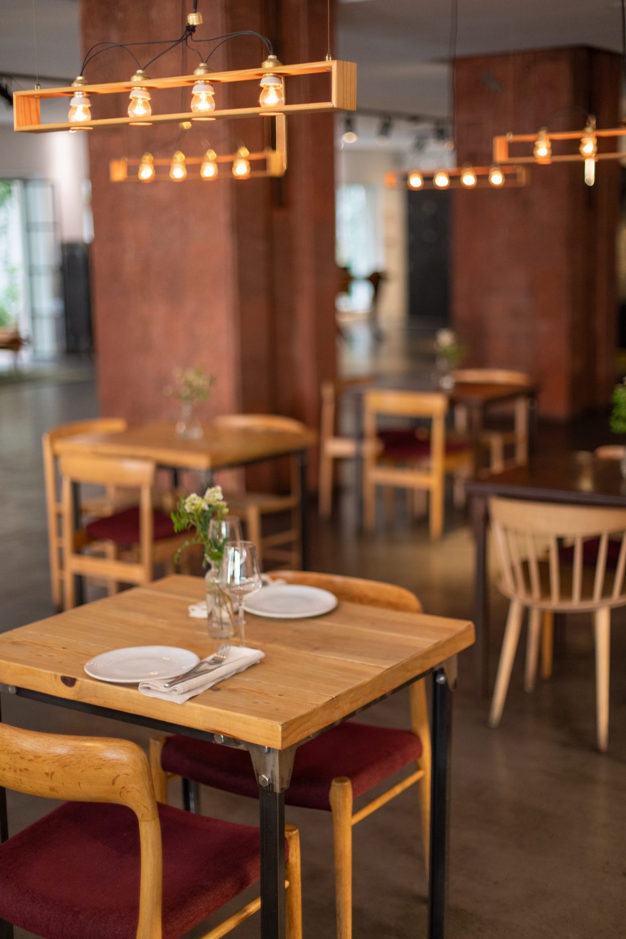 The 7 Kitchen & Bar dining room, with wooden tables set for two under hanging bulb light fixtures and burgundy-cushioned chairs.