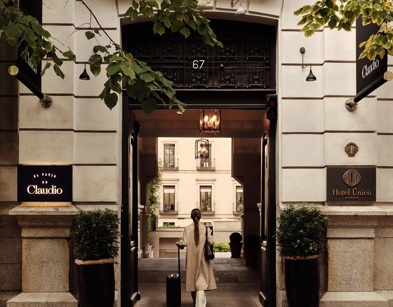The street entrance at number 67, with Hotel Único and El Patio de Claudio signs flanking a tall gateway that opens onto an inner patio.