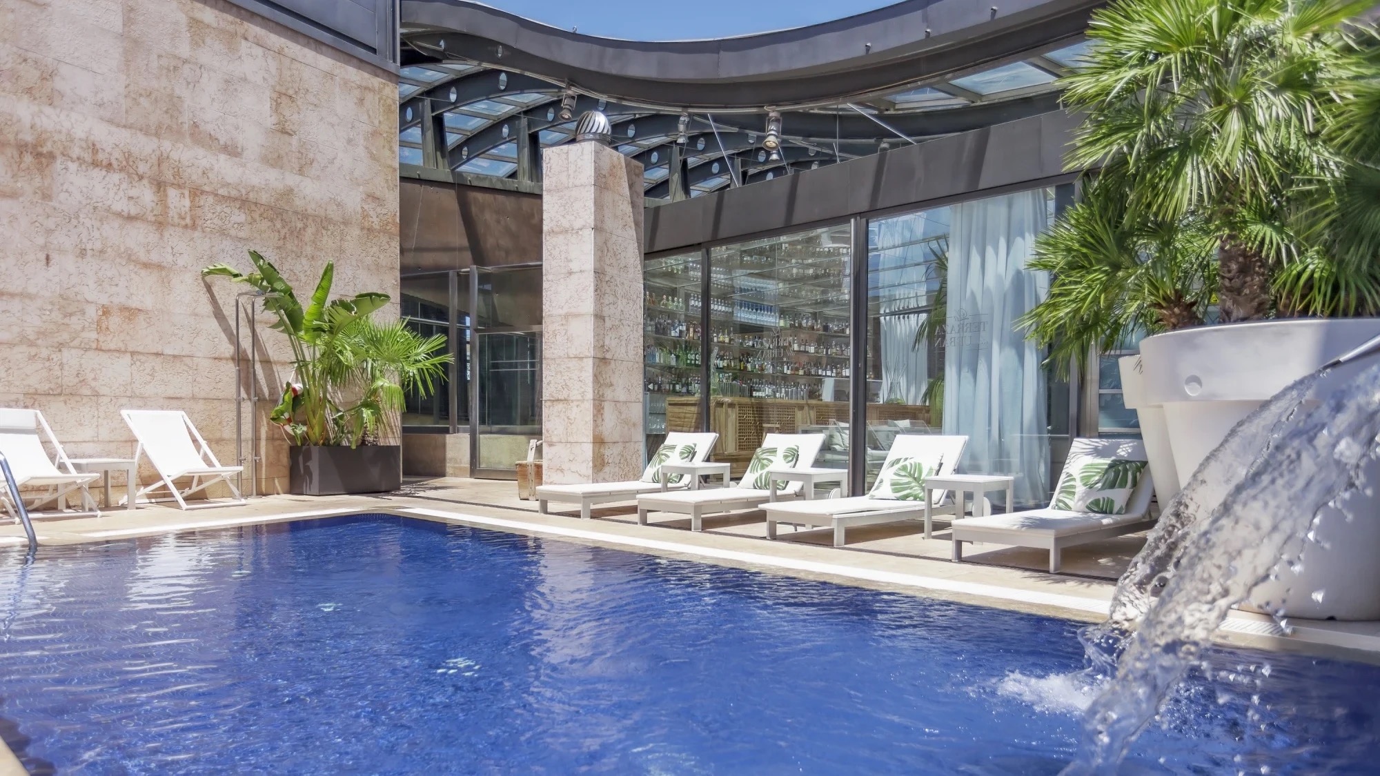 The rooftop pool at Hotel Urban, loungers along one side and the glass-walled terrace bar behind.
