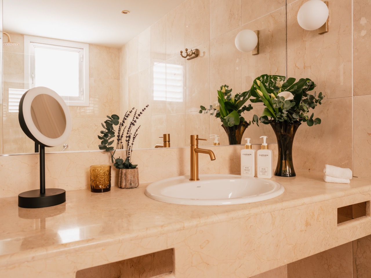 Marble bathroom with gold fixtures, freestanding vanity mirror and fresh flowers