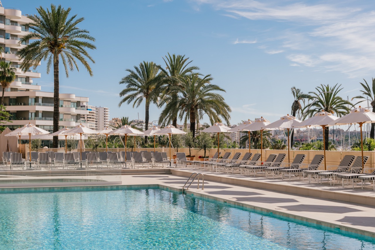 Outdoor pool lined with striped loungers and umbrellas, palm trees in the background