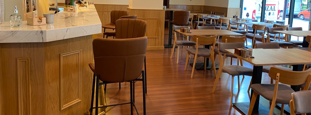 A wood-panelled marble-topped bar counter with high stools next to wooden dining tables and chairs in the hotel's cafeteria.