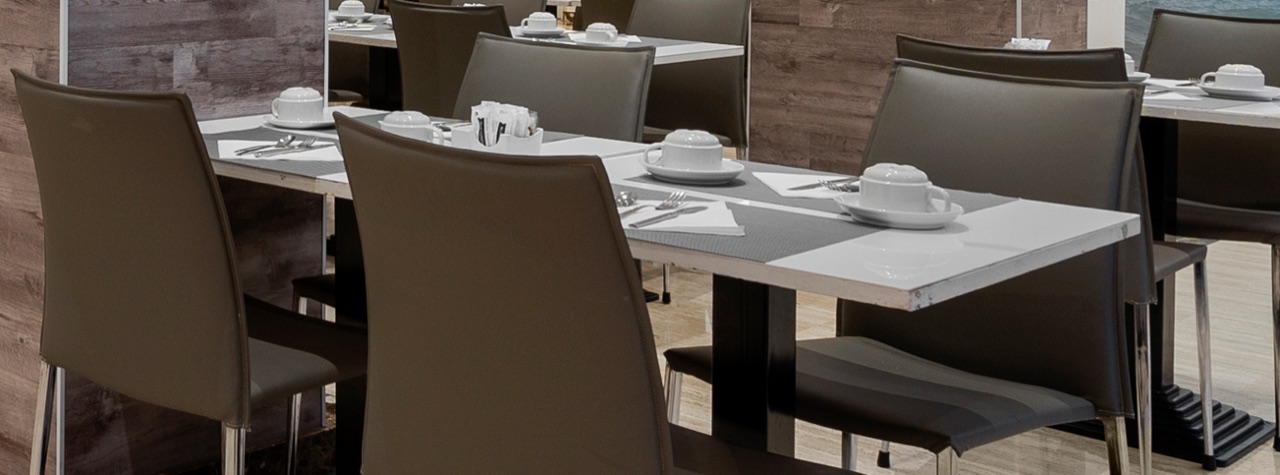 Set tables in the hotel's dining room with white place mats, coffee cups and cutlery, and dark leather chairs.