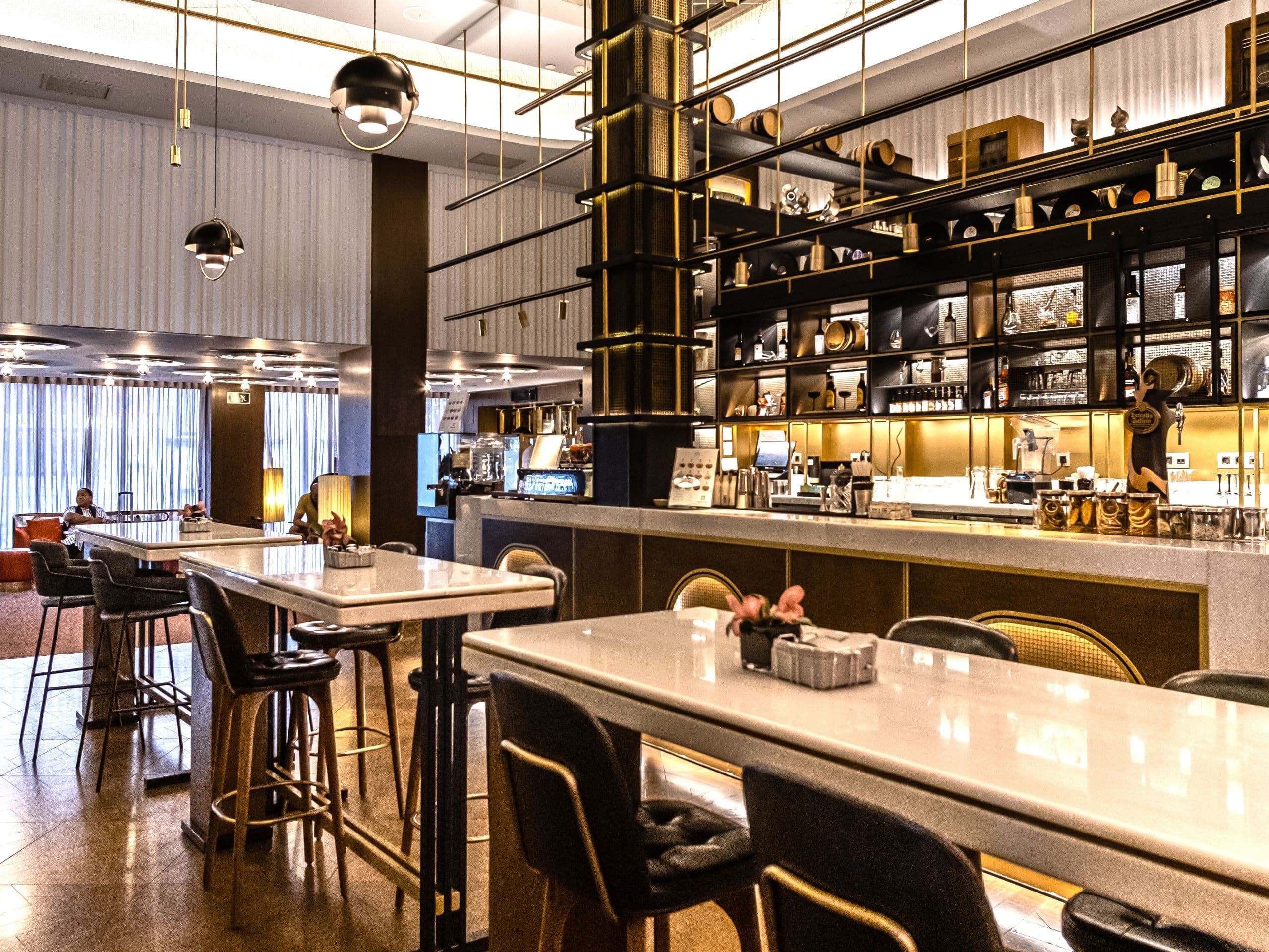 Bar area with marble-topped high tables, leather stools and a brass-framed back bar.