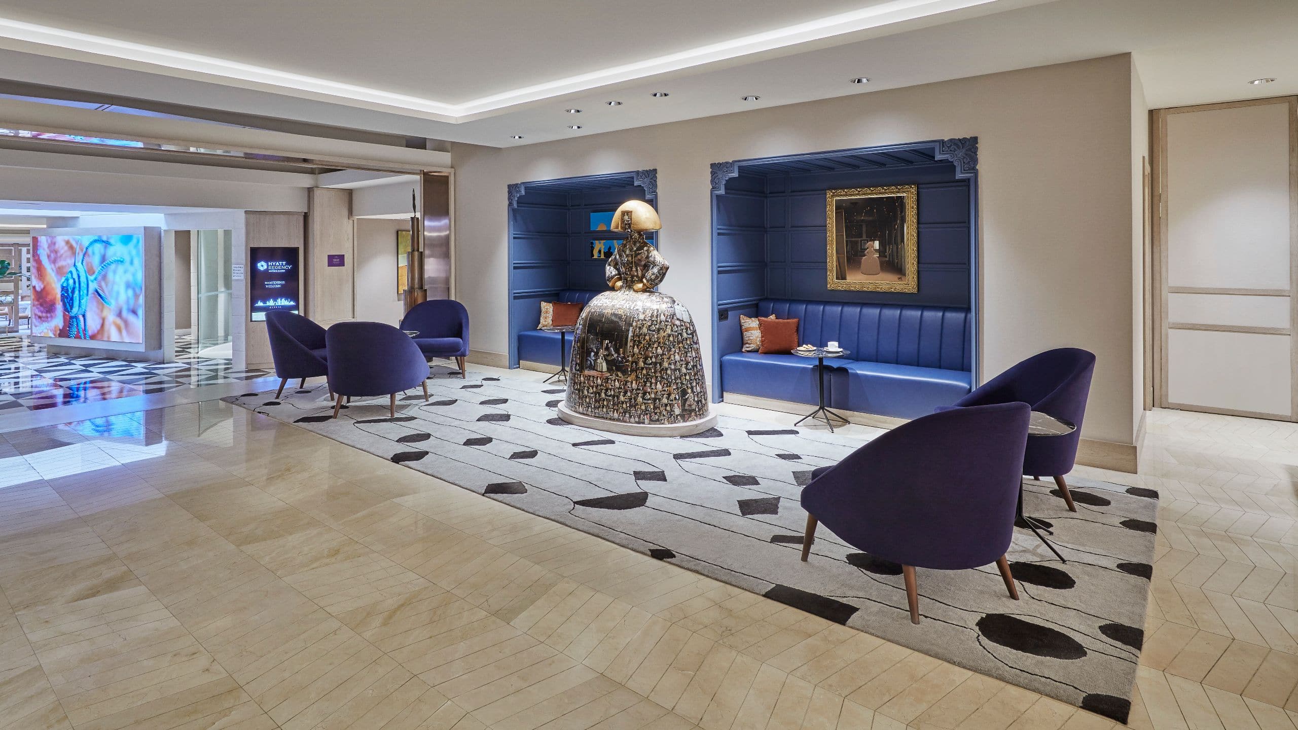 Lobby lounge with purple armchairs, blue panelled seating nooks and a Menina sculpture on a patterned rug.